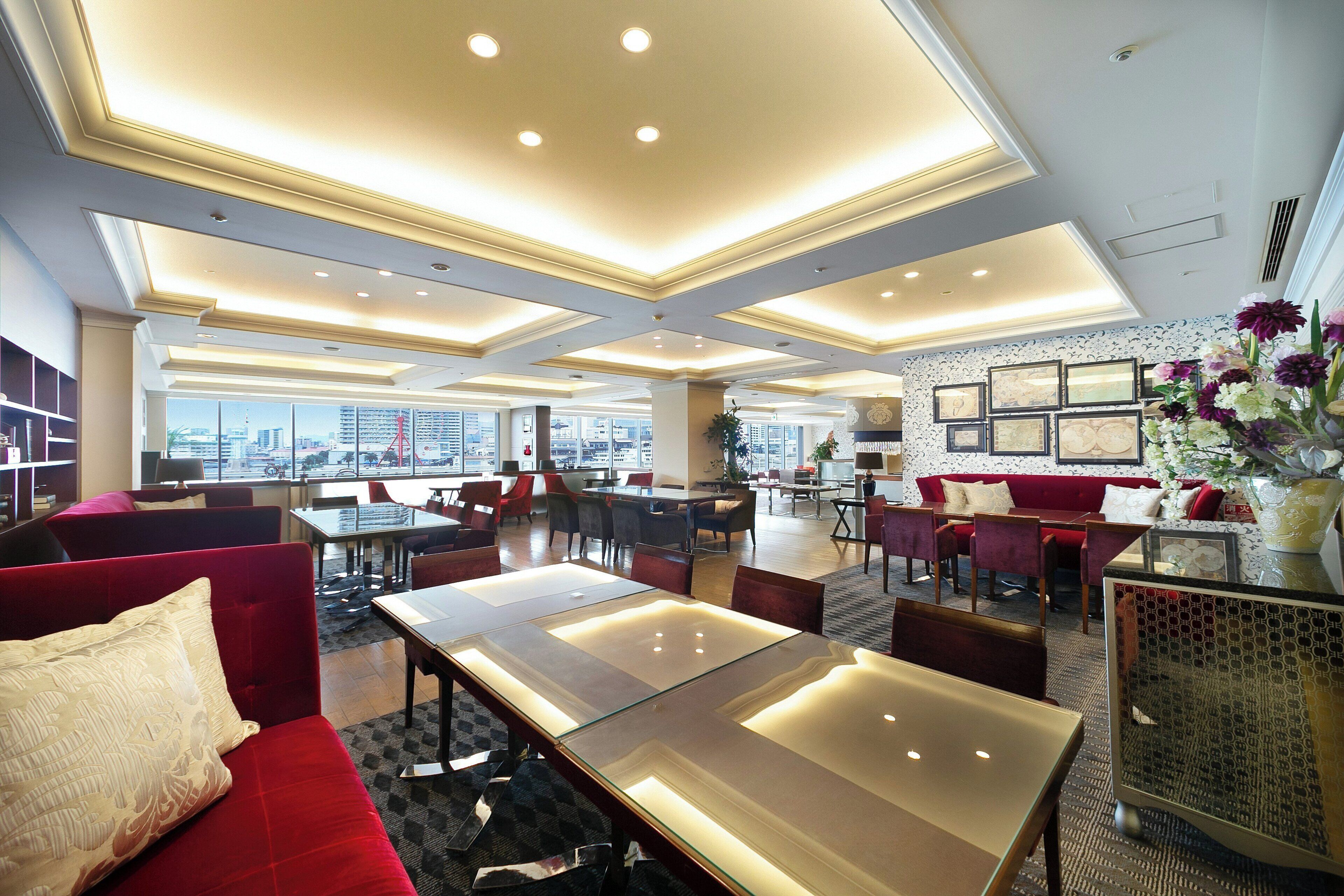 A spacious hotel lobby with a high ceiling, multiple seating areas, and a view of the cityscape through large windows.
