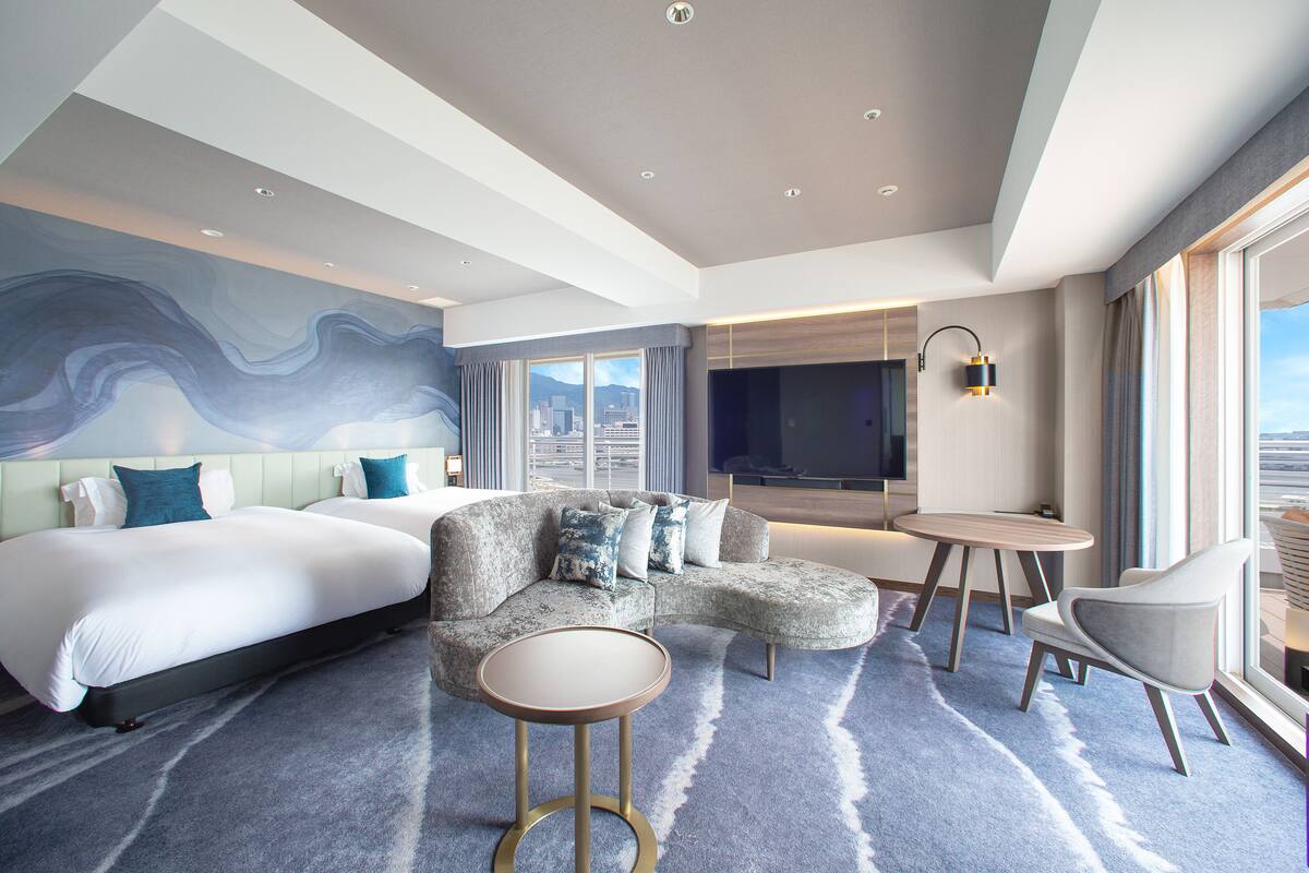 Una habitación de hotel moderna con una cama grande, un sofá, una mesita y un televisor.