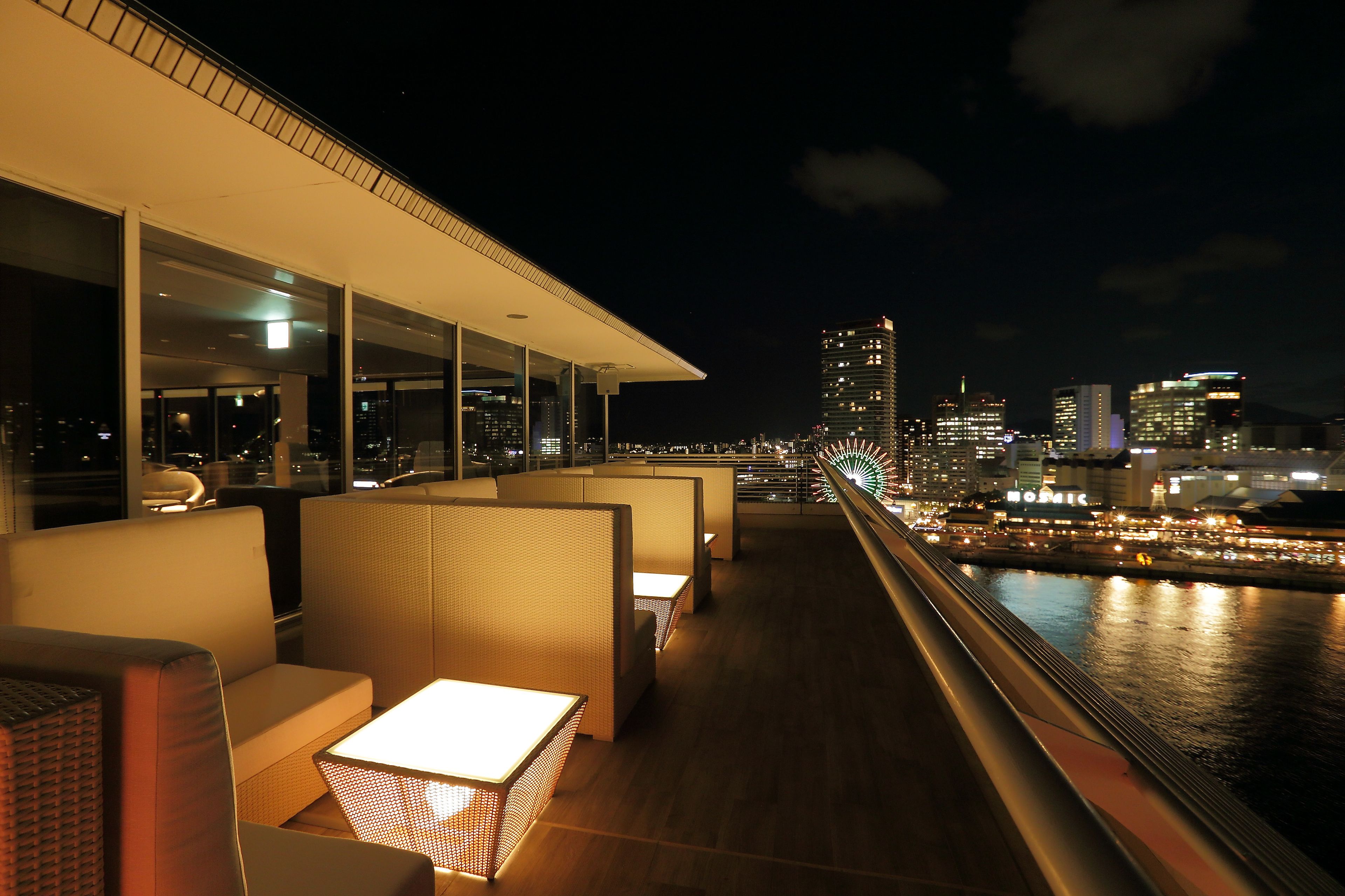 A rooftop bar with seating and a view of the city skyline at night.
