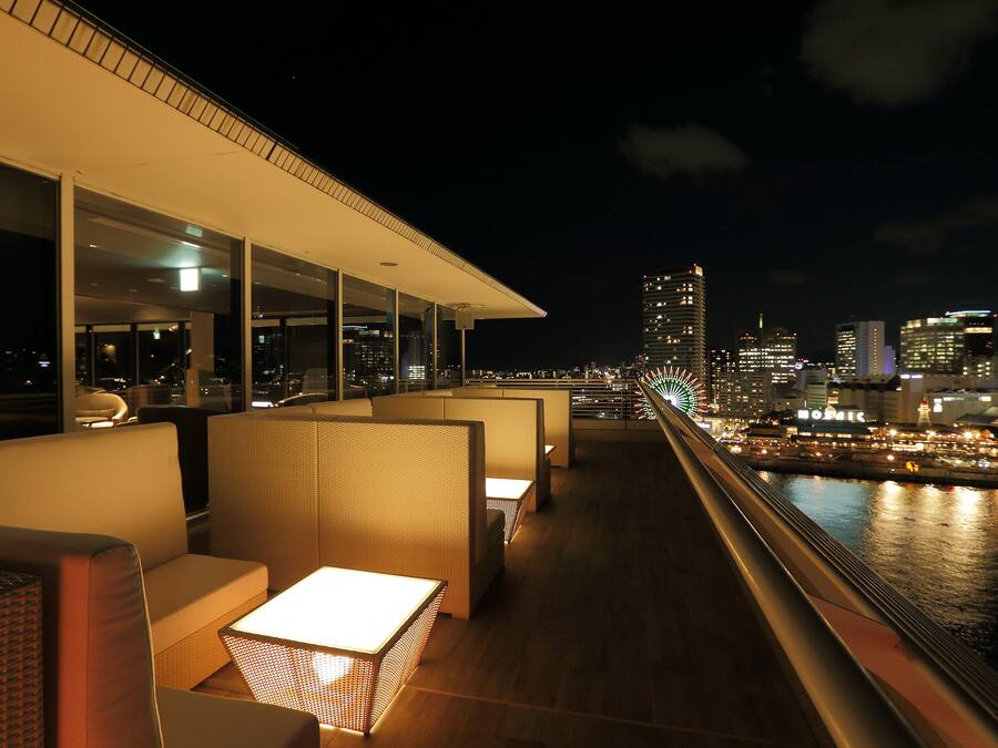 A rooftop bar with seating and a view of the city skyline at night.
