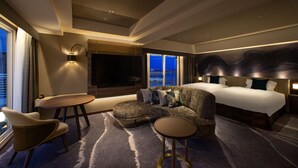 Una habitación de hotel moderna con un sofá curvo, una mesa redonda, una cama grande y vistas a la ciudad a través de la ventana.