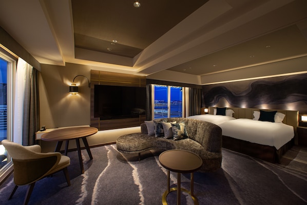 Una habitación de hotel moderna con un sofá curvo, una mesa redonda, una cama grande y vistas a la ciudad a través de la ventana.
