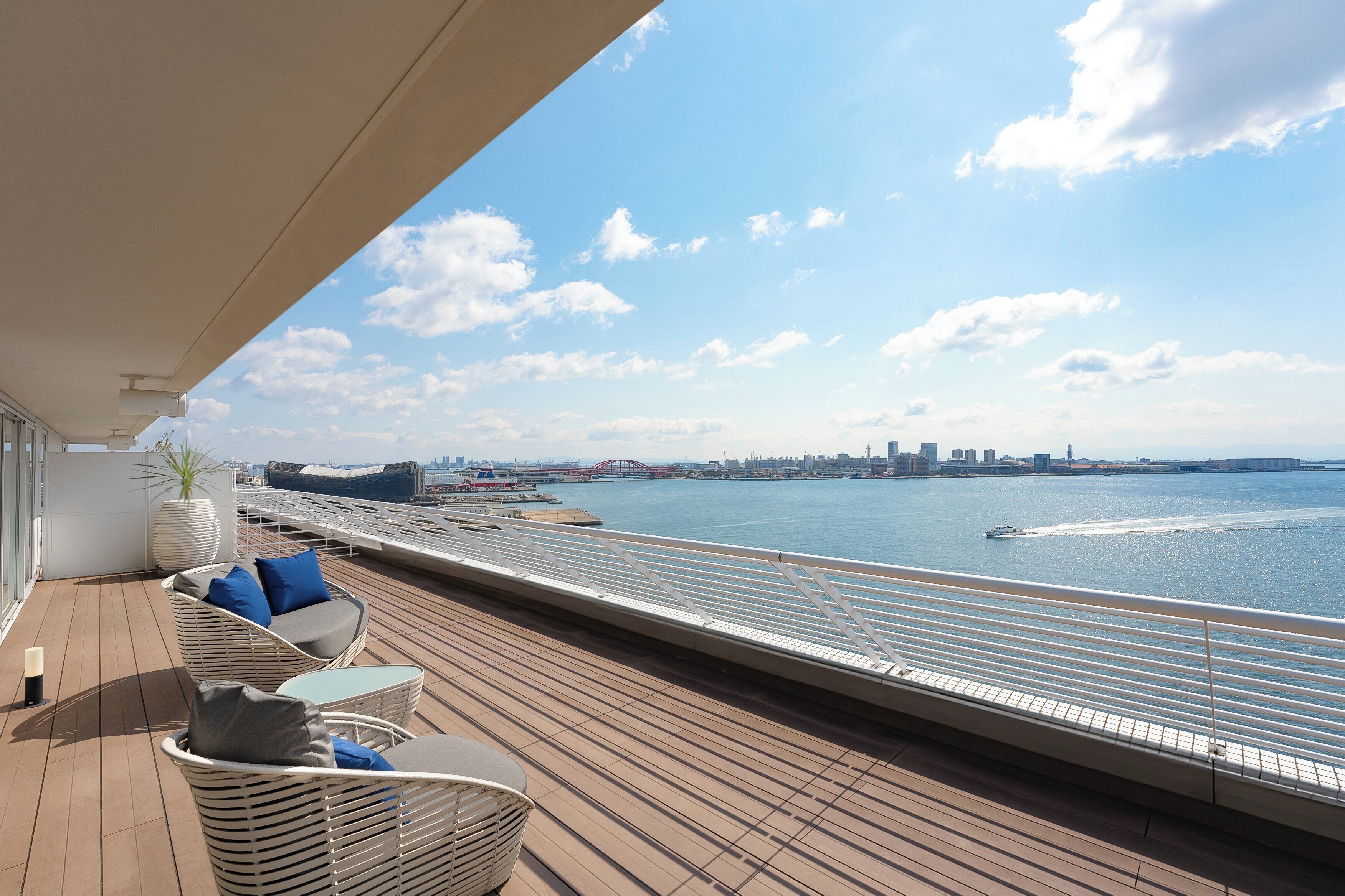 A deck with wicker furniture and a view of the water and city skyline.