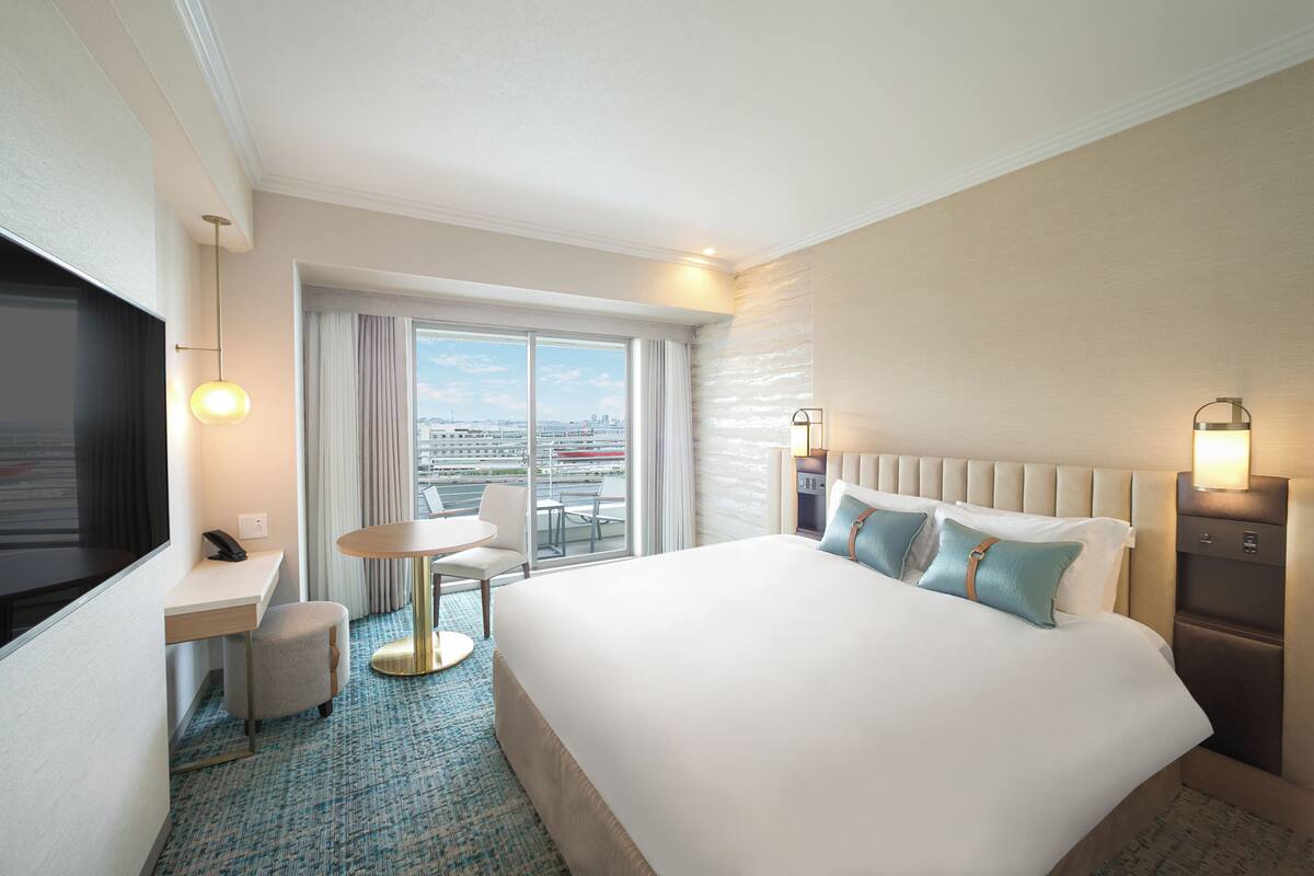 Habitación de hotel con una cama grande, un escritorio, una silla, una mesita pequeña y un televisor.