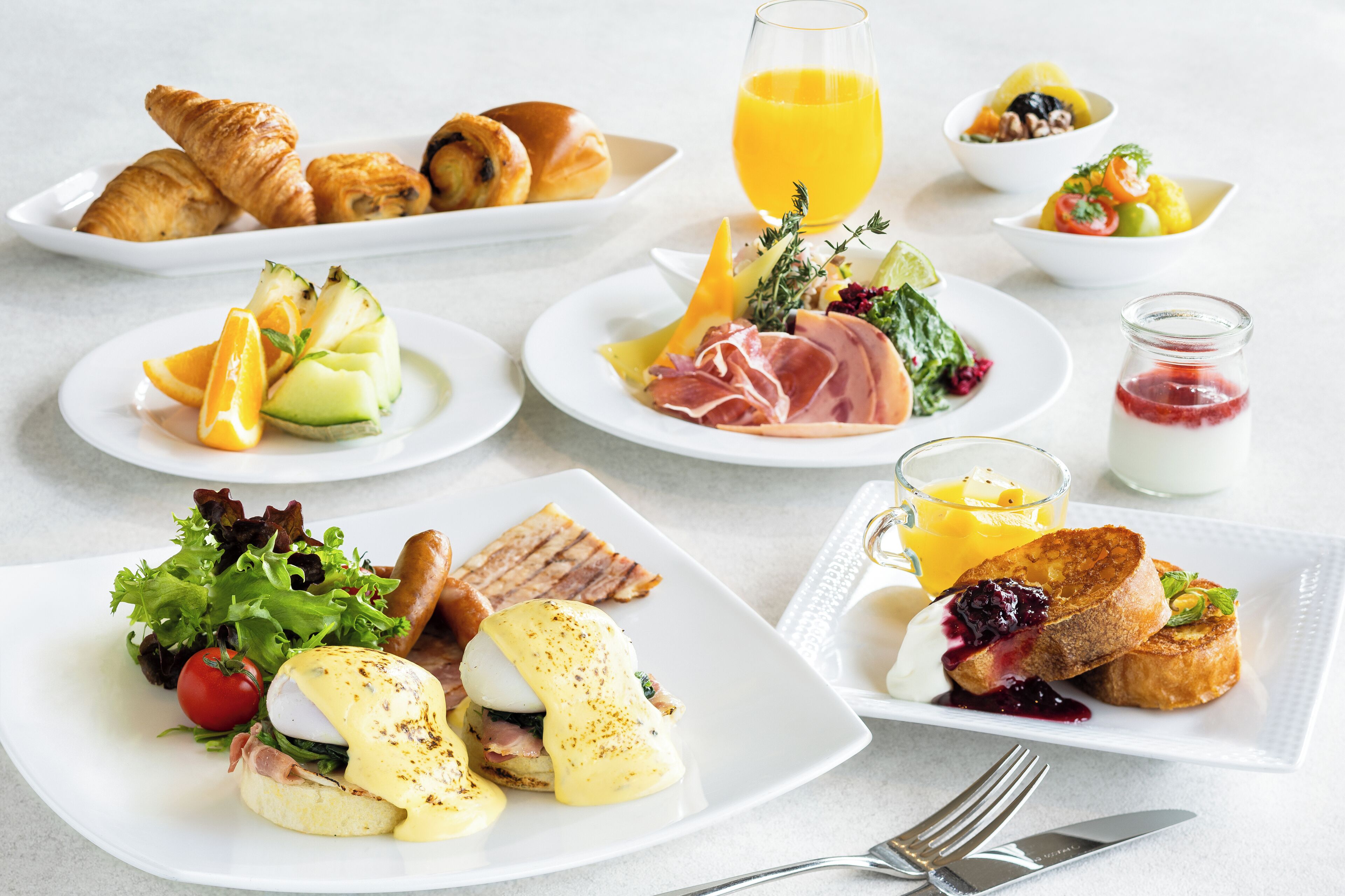 Un buffet de petit-déjeuner comprenant des croissants, des fruits, des œufs et diverses salades.