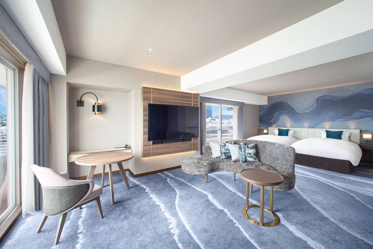 Una habitación de hotel moderna con una cama grande, un sofá, una mesita y un televisor montado en la pared.