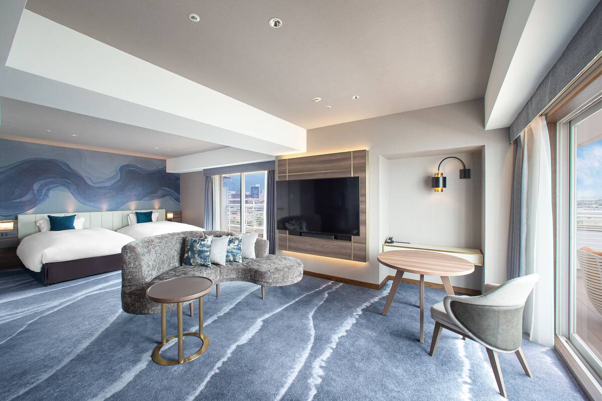 Una habitación de hotel moderna con una cama grande, un sofá, una mesita y un televisor.