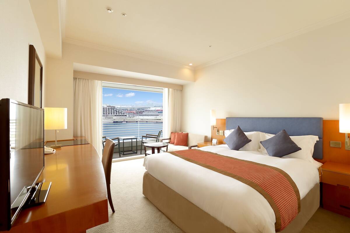 Una habitación de hotel con una cama, un escritorio, una silla, un televisor y vistas a la ciudad.