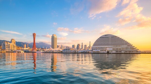 A waterfront cityscape with modern architecture, including a distinctive red tower and a large white building with a curved roof. - Kobe MerikenPark Oriental Hotel (Kobe)