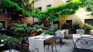 Une terrasse extérieure avec des tables et des chaises, entourée de plantes en pot et d’arbres.