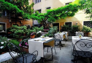 An outdoor patio with tables and chairs, surrounded by potted plants and trees. - Sina Palazzo Sant'Angelo (Venice)