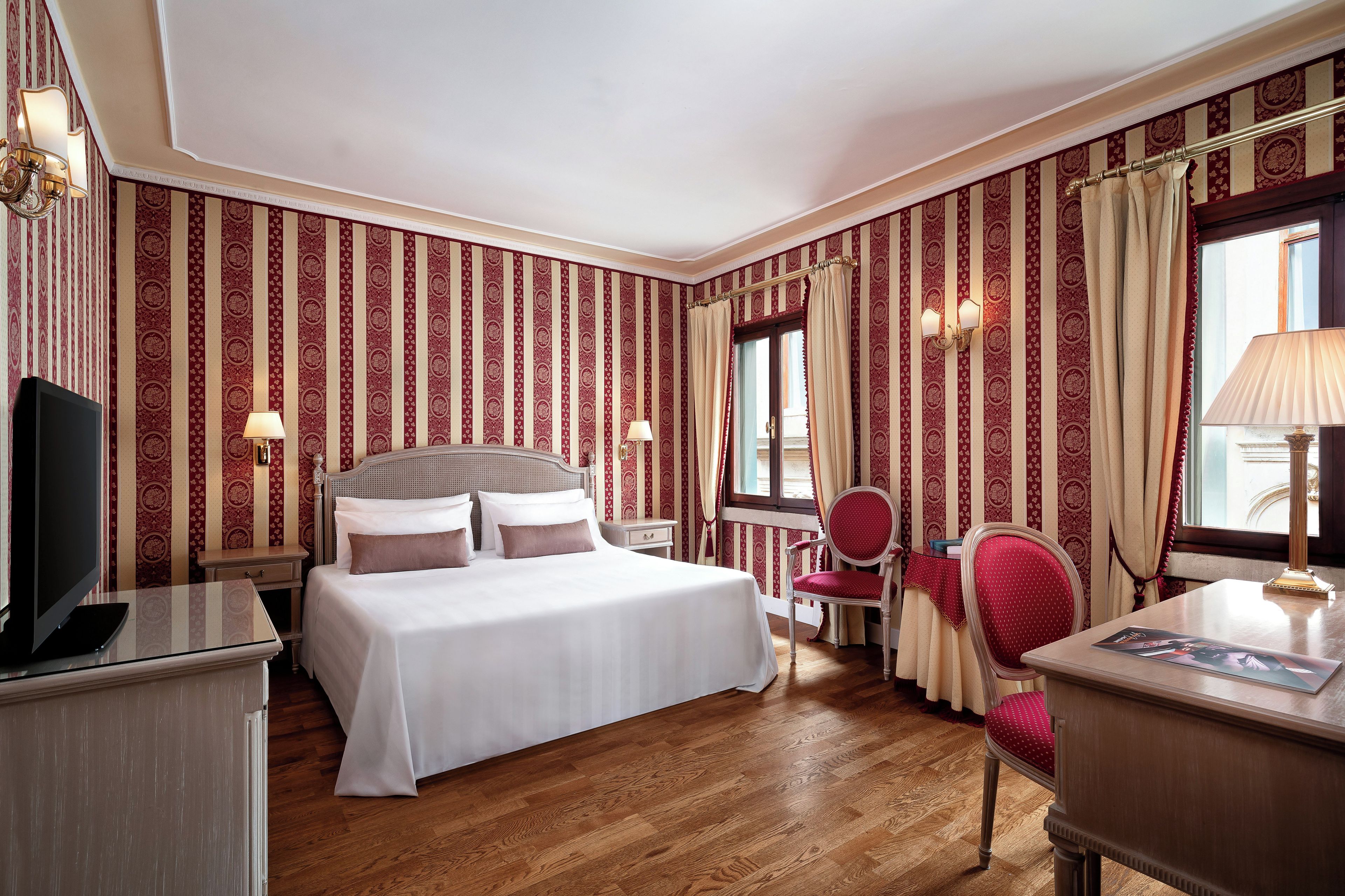Habitación de hotel con cama, escritorio, silla, televisor y ventana con cortinas.