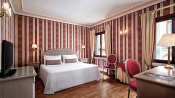 Habitación de hotel con cama, escritorio, silla, televisor y ventana con cortinas.