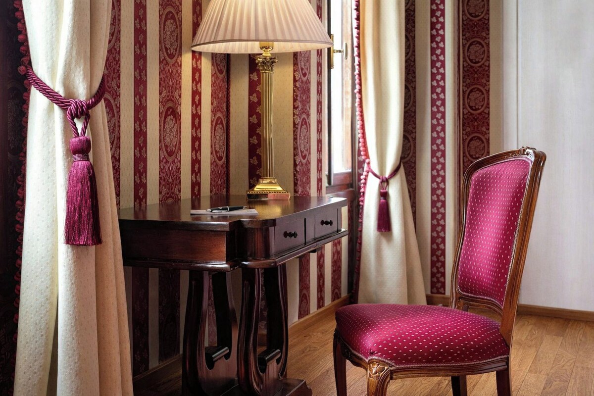 A room with a desk, a lamp, a chair, and patterned curtains.