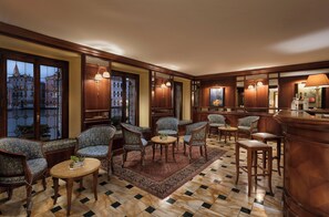 Un hall de hotel con sillas de estampado llamativo, una zona de bar y un ventanal con vistas a edificios.