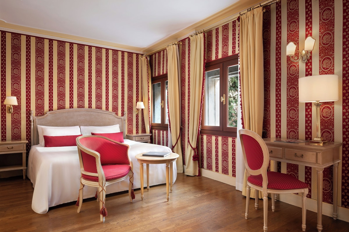 A hotel room with a bed, two chairs, a desk, and a window with curtains.