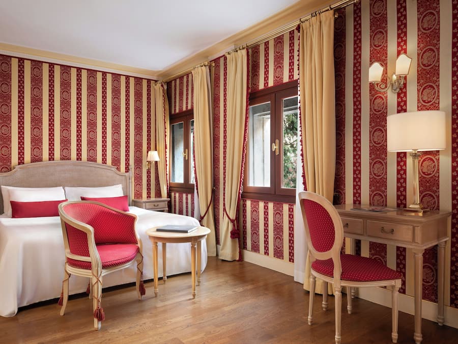 Habitación de hotel con cama, dos sillas, escritorio y ventana con cortinas.
