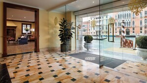 A hotel lobby with a checkered floor, a seating area, and a view of a historic building through glass doors. - Sina Palazzo Sant'Angelo (Venice)