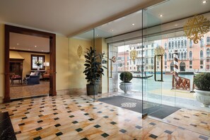 A hotel lobby with a checkered floor, a seating area, and a view of a historic building through glass doors. - Sina Palazzo Sant'Angelo (Venice)