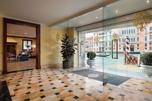 Um hall de hotel com chão quadriculado, área de estar e vista para um edifício histórico através de portas de vidro.
