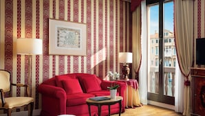 A hotel room with a red sofa, a wooden chair, a small table with a plant, a framed map on the wall, and a balcony with curtains. - Sina Palazzo Sant'Angelo (Venice)