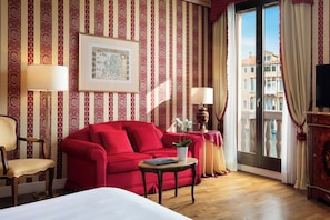 A hotel room with a red sofa, a wooden chair, a small table with a plant, a framed map on the wall, and a balcony with curtains. - Sina Palazzo Sant'Angelo (Venice)
