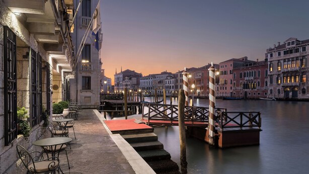 A waterfront hotel with outdoor seating, a red carpet, and a view of the water and city buildings. - Sina Palazzo Sant'Angelo (Venice)