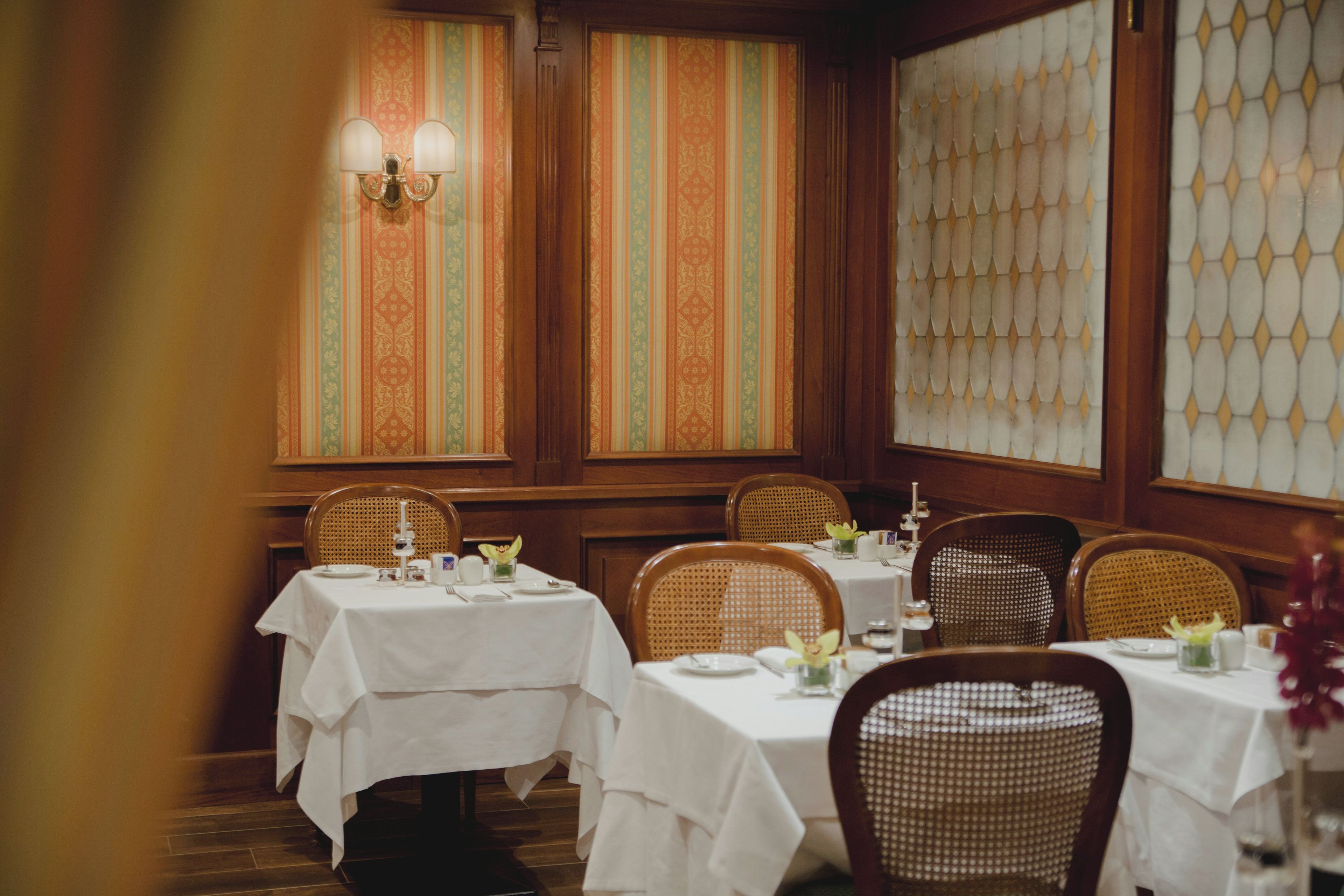Ein Restaurant mit mehreren Tischen, Korbstühlen und Wandpapier mit Muster.