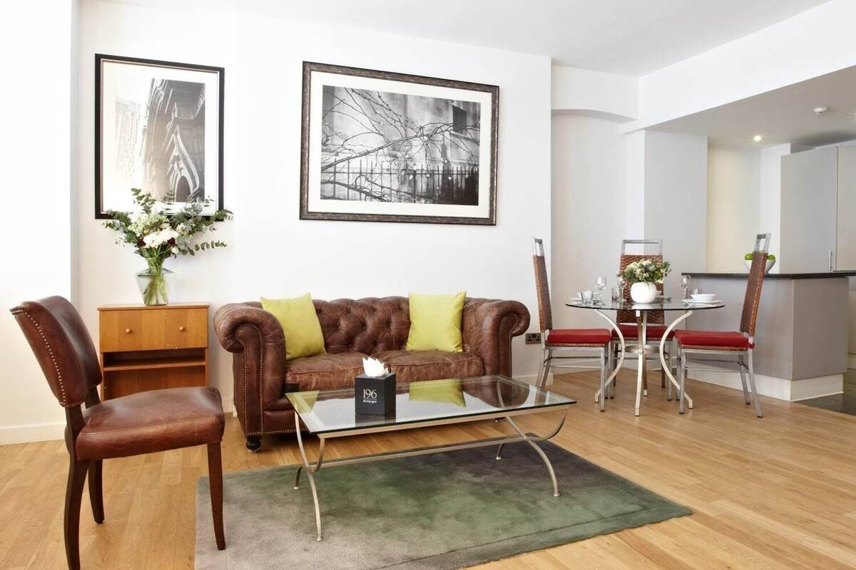 A modern living room with a leather sofa, a glass coffee table, and a dining area with a metal table and chairs.
