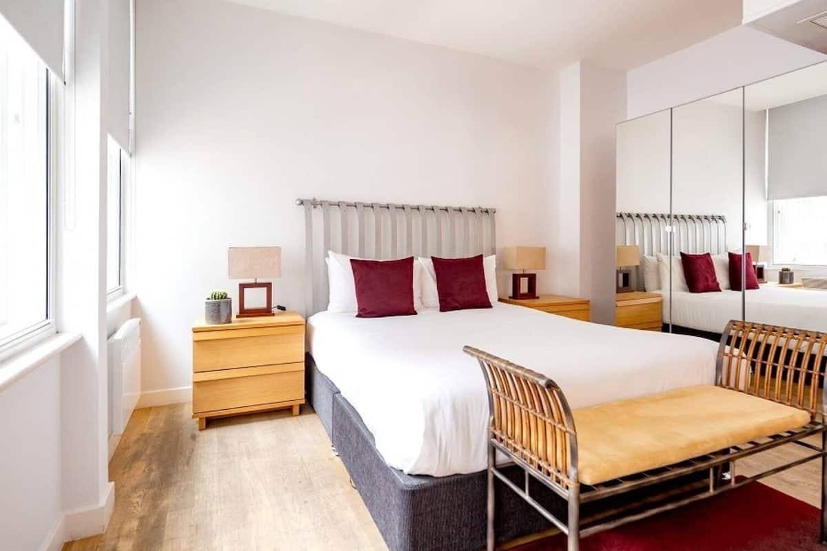 A modern hotel room with a large bed, bedside tables, a chair, a mirror, and a wardrobe.
