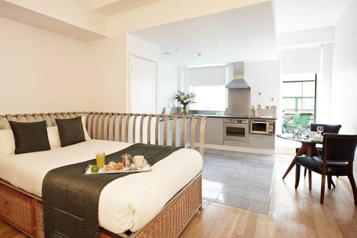 A hotel room with a bed, breakfast tray, kitchenette, dining area, and a view of the outside.