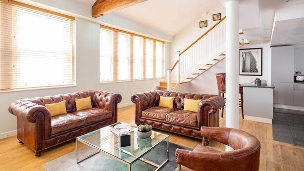 Ein geräumiges Wohnzimmer mit Ledersofas, einem Glastisch und einer Treppe, die zur Küche führt.