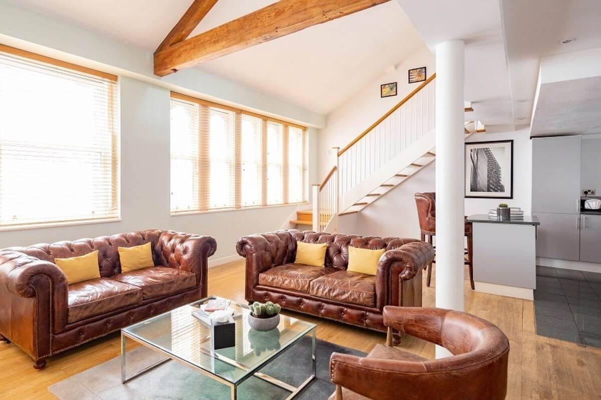 A spacious living room with leather sofas, a glass coffee table, and a staircase leading to a kitchen.