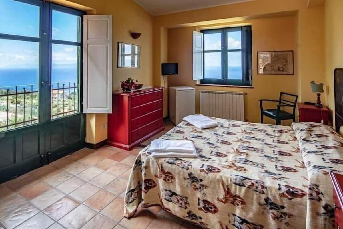 Ein Schlafzimmer mit Bett, Schminktisch, Stuhl, Fenster mit Ausblick und Heizkörper.