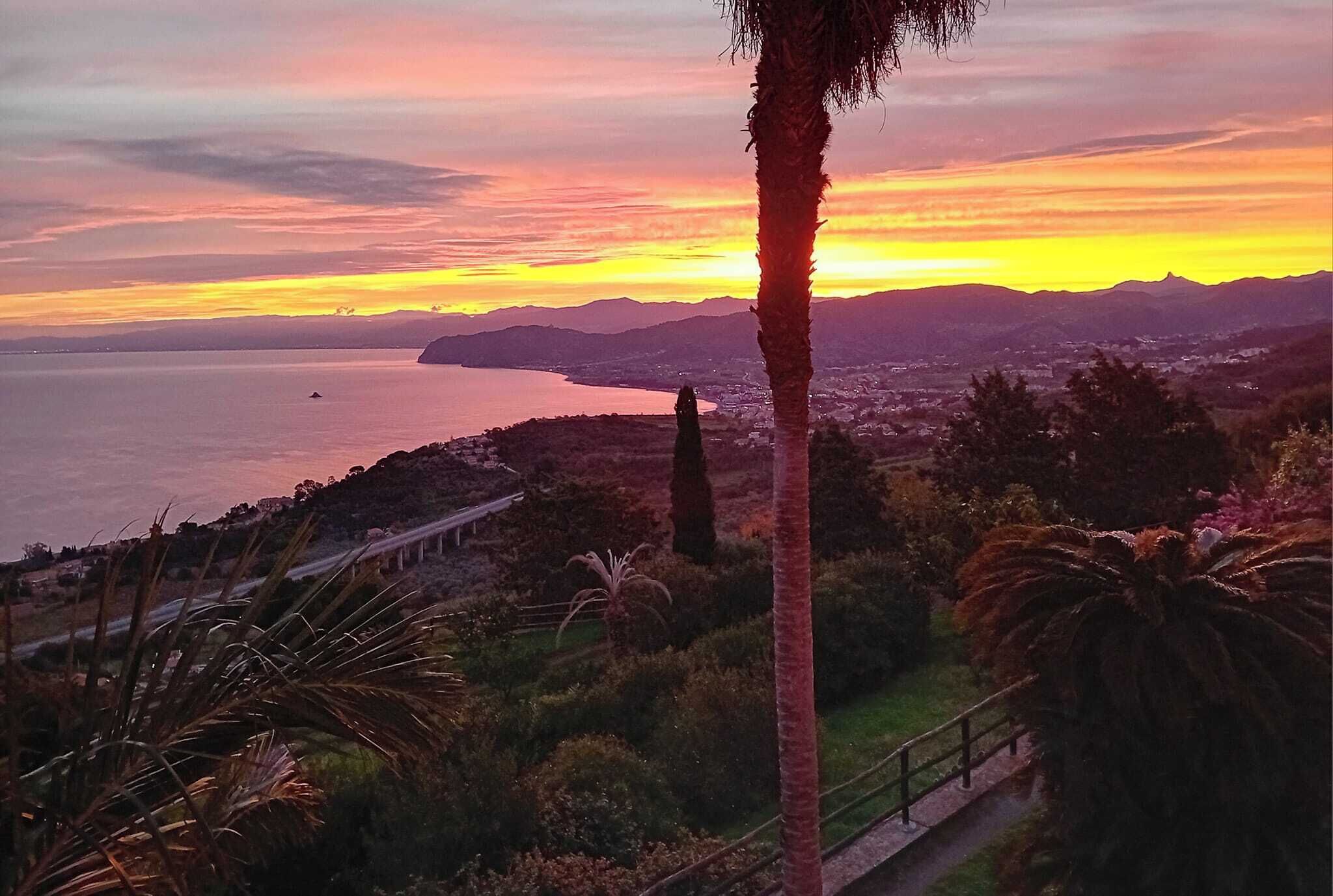 A coastal landscape with a sunset, palm trees, and a road leading to a town.
