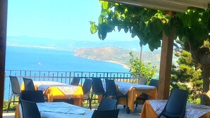Un área de comedor al aire libre con mesas y sillas, con vistas a un paisaje costero.