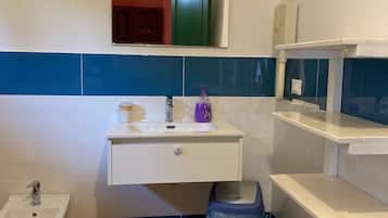 Une salle de bain avec un lavabo blanc, un miroir, un bidet et une poubelle.