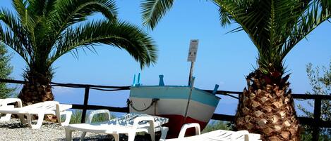 A beachside area with a row of white plastic lounge chairs, a small boat, and palm trees.