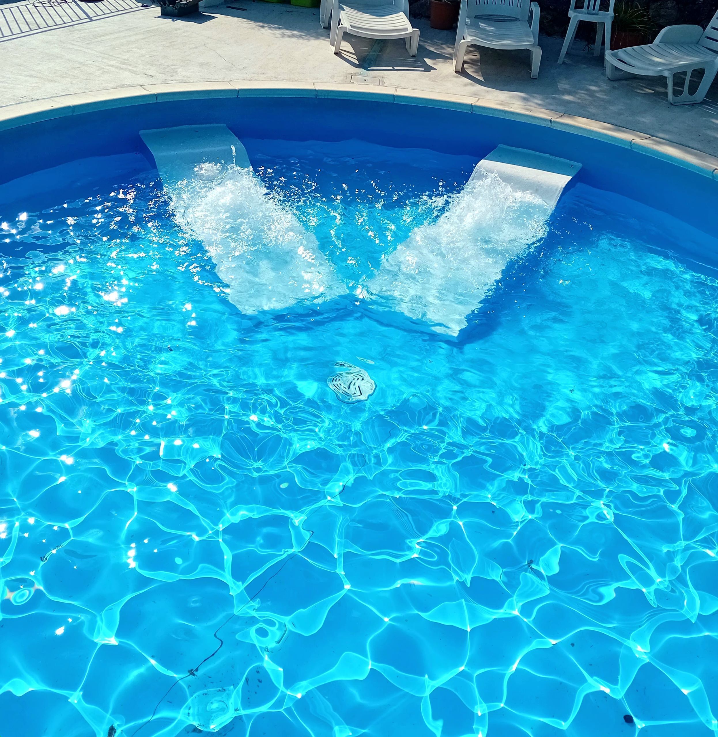 En klarblå pool med synliga vattenspridningar och en ensam fontän i mitten.