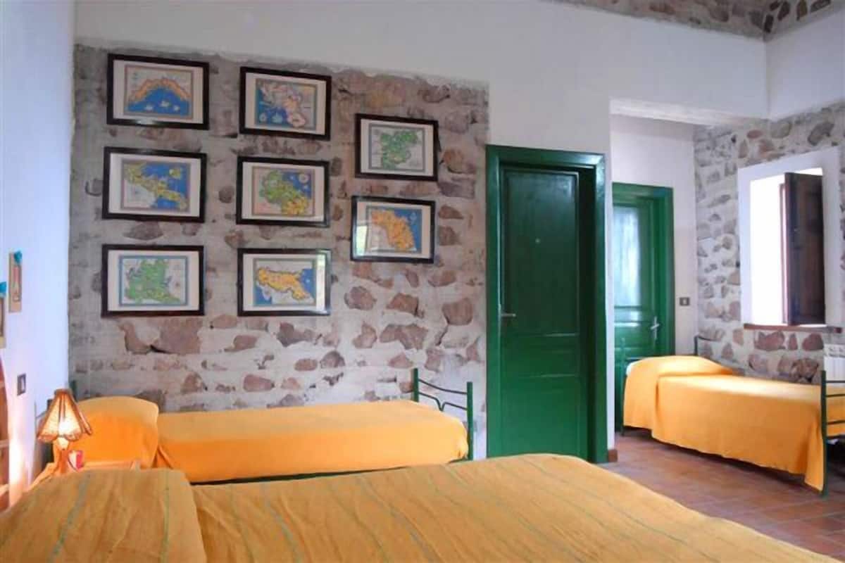 Ein Zimmer mit zwei Betten, einer Steinsäule und gerahmten Karten.