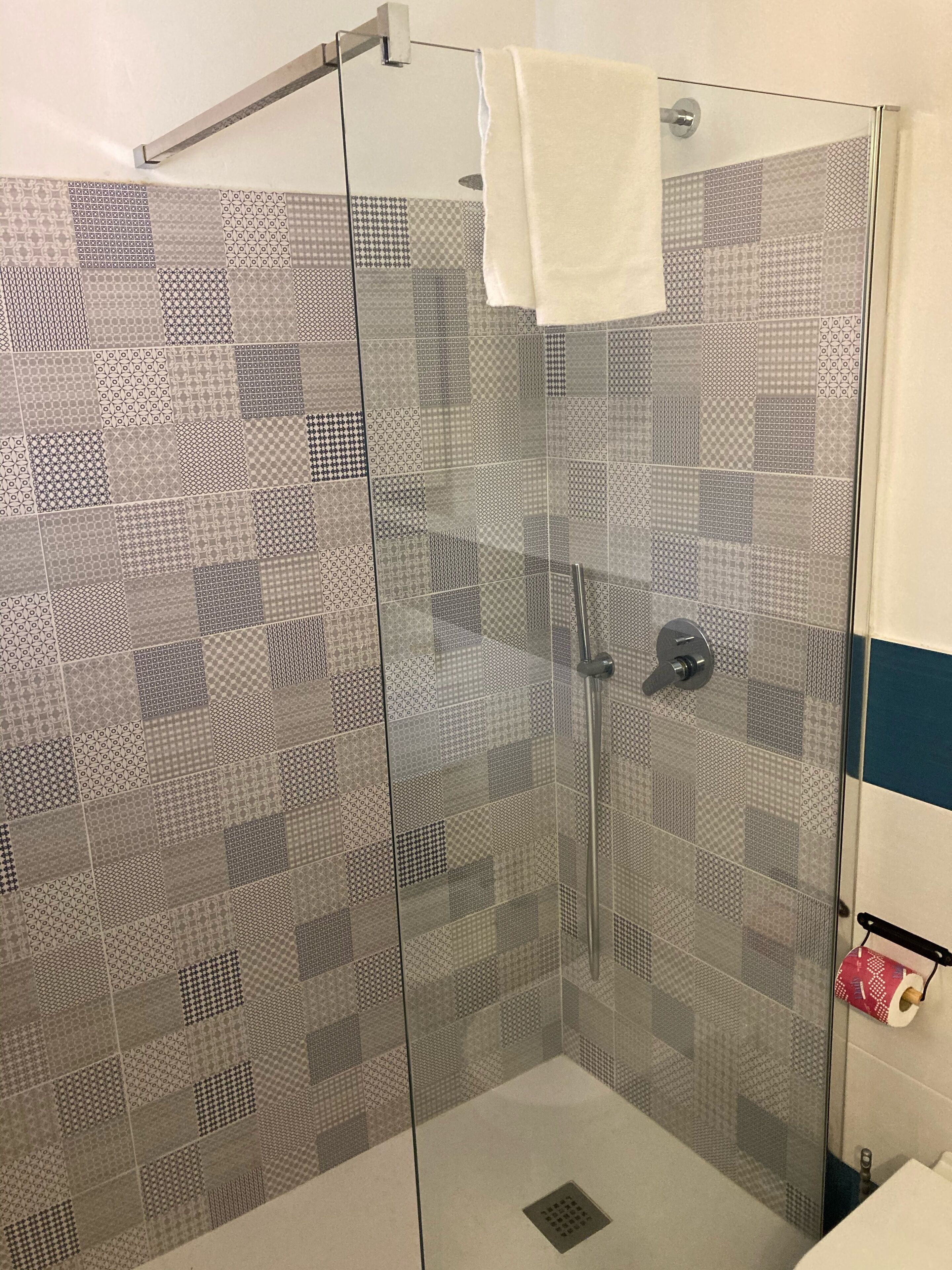 A shower with a glass door, patterned tiles, and a towel hanging on the door handle.