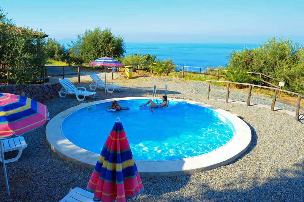 Une piscine ronde où se trouvent deux personnes, entourée de chaises longues blanches et de parasols.