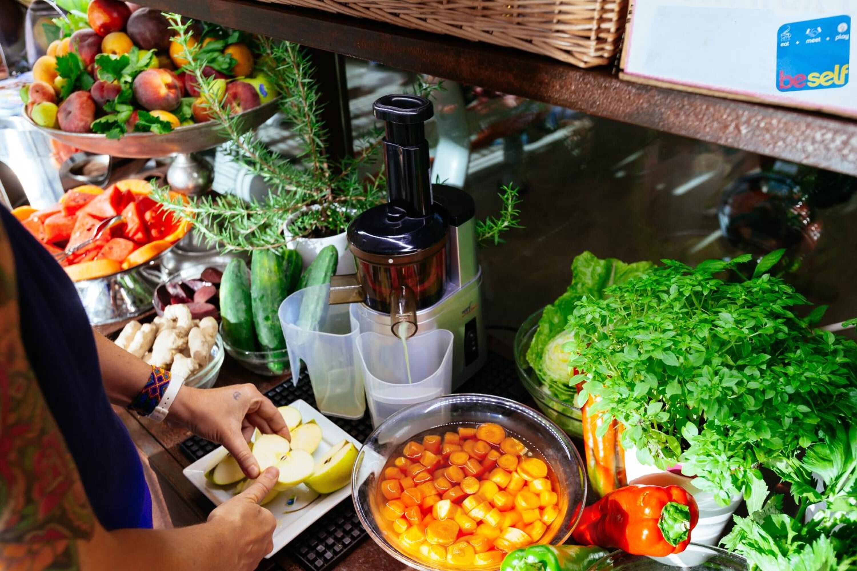 A kitchen counter with various fruits and vegetables, a juicer, and a person preparing food.
