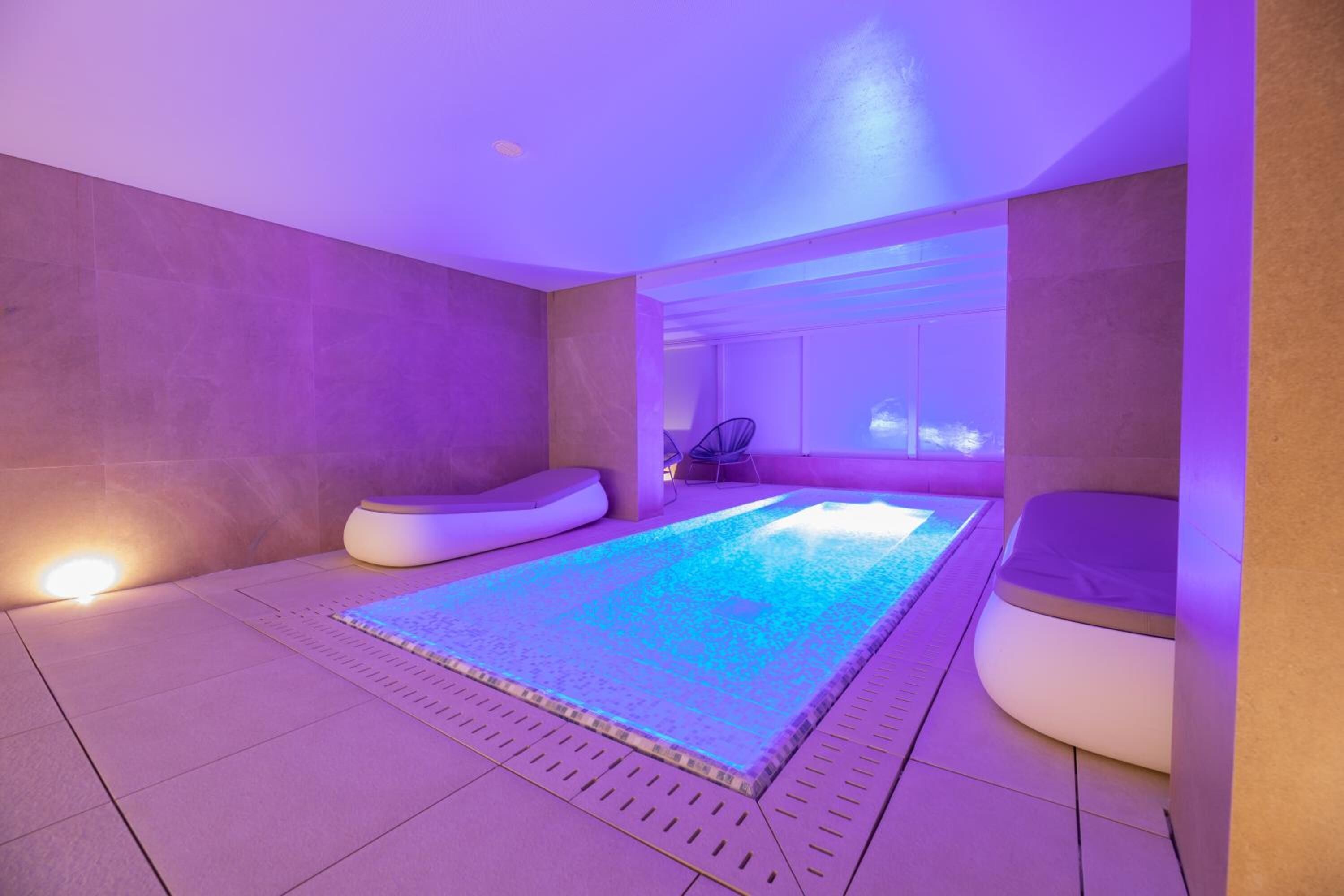 A modern spa area with a large heated pool, cushioned seating, and a view of the sky.