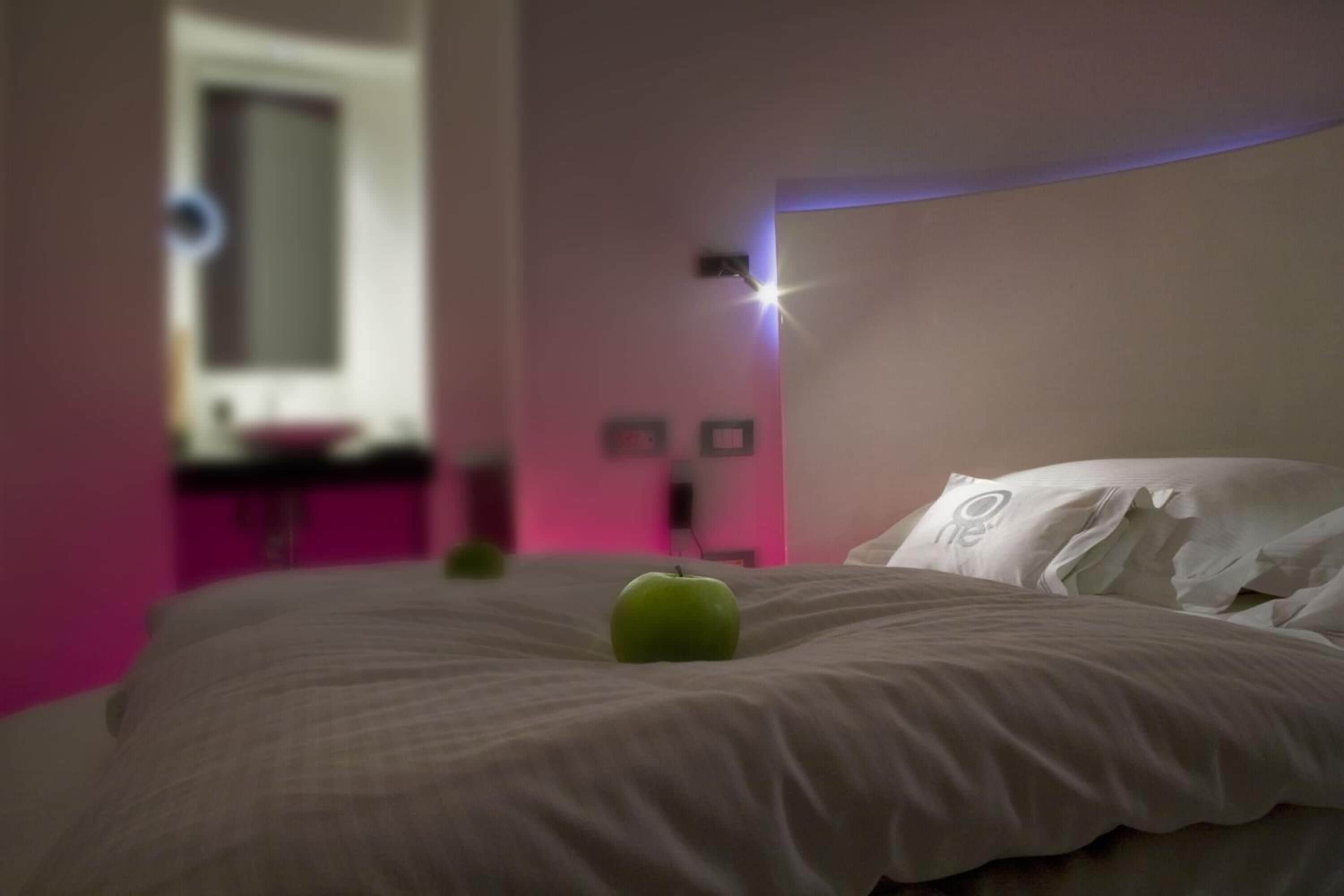 A neatly made bed with pillows and a green apple on it.