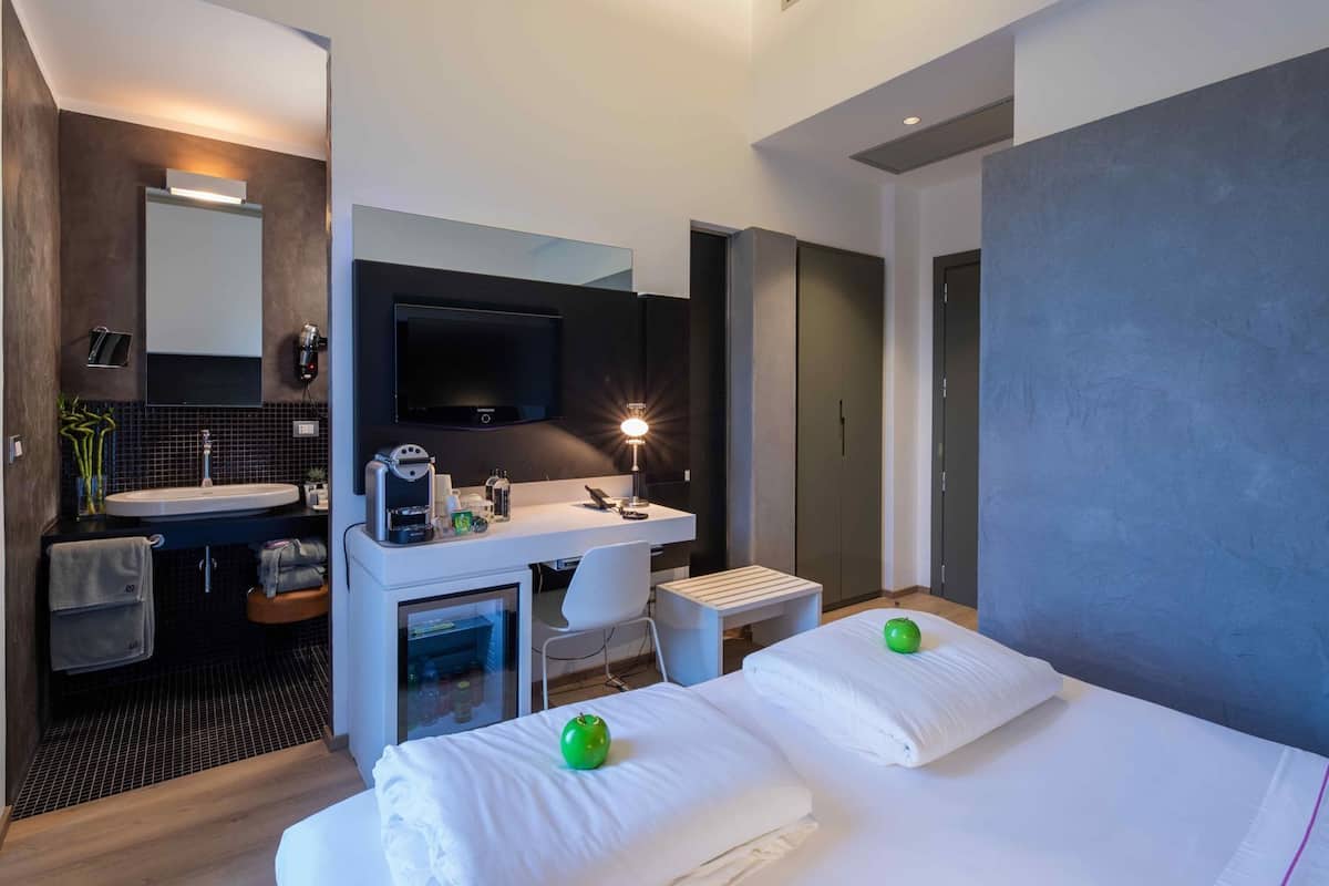Una camera d'albergo moderna con un letto, comodini, una scrivania con una sedia, una TV e un bagno con lavandino e specchio.