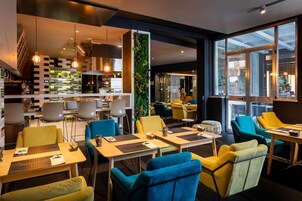 Un restaurante moderno con sillas amarillas y azules, mesas con manteles individuales y una cafetera espresso visible.