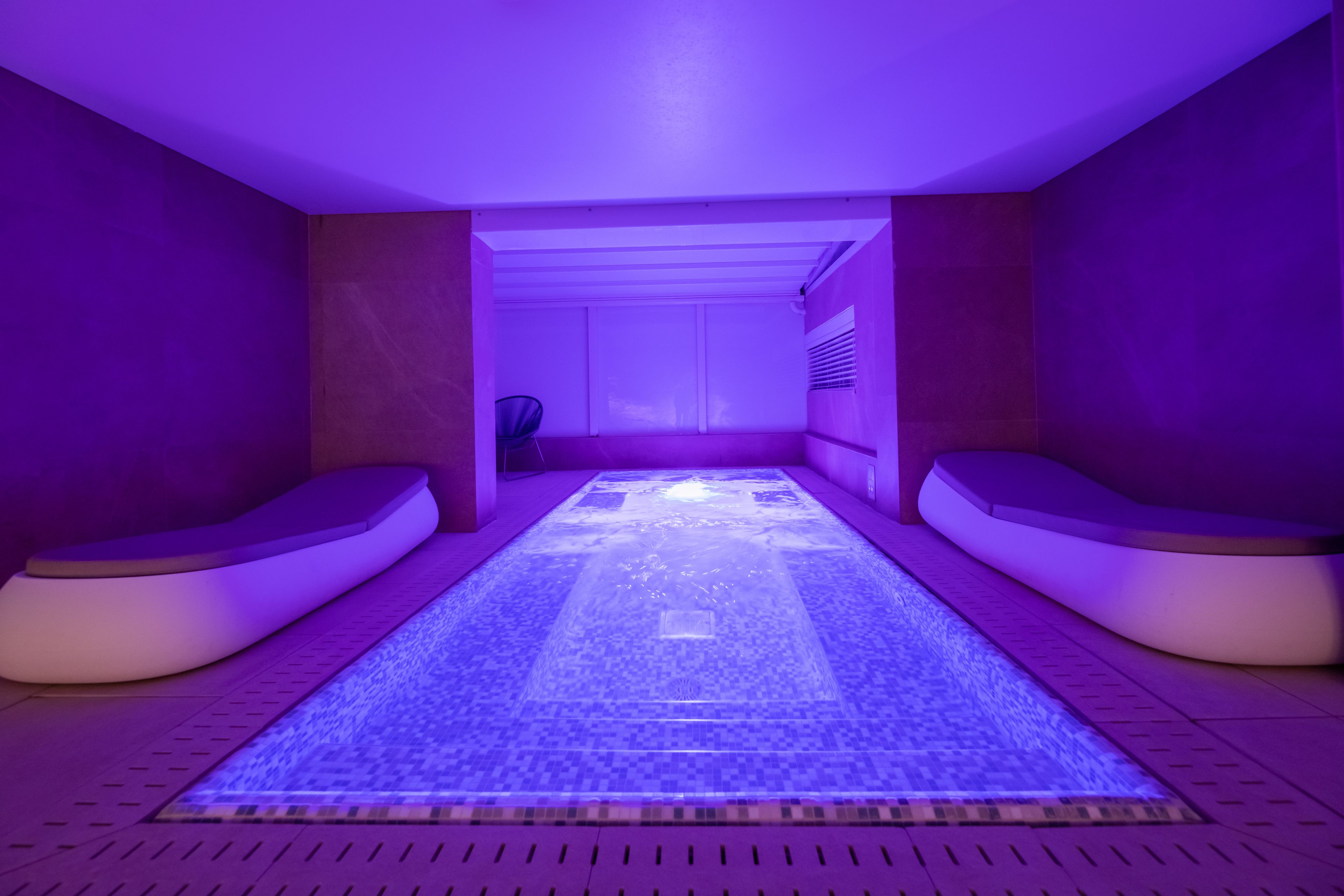 A spa room with a central heated floor, two seating areas, and a ceiling light.