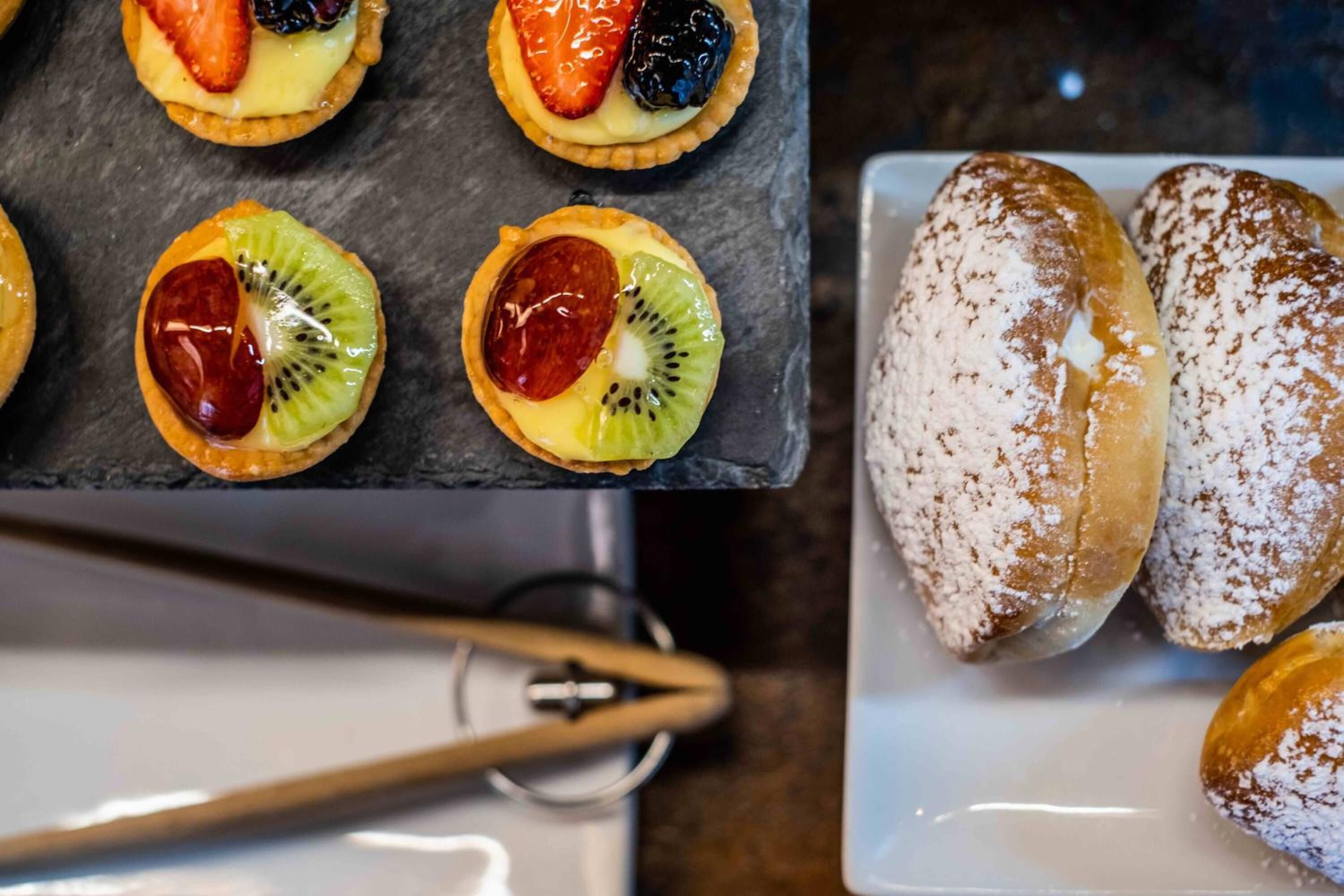 Una variedad de postres, incluyendo tartas con fruta y rosquillas espolvoreadas, sobre un plato.
