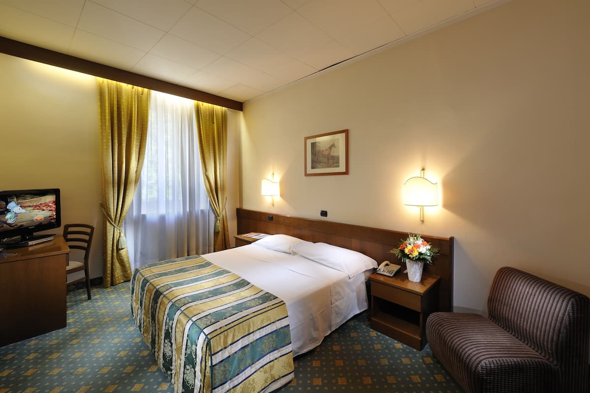Ein Hotelzimmer mit Bett, Schreibtisch, Stuhl, Nachttisch mit Lampe und fest montiertem Telefon.